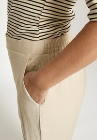 Heledat beeži, elastse vöökohaga püksid küljetaskutega, mis on valmistatud pehmest, tekstuuriga kangast. Sobitatud musta-beeži triibulise topiga.