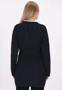 Lungo cardigan blu navy con un design strutturato a costine, vita cinturata e apertura frontale. Presenta motivi verticali e maniche lunghe.
