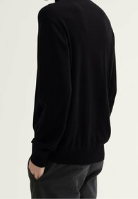 Svart stickad tröja med avslappnad passform, ribbade ärmslut och nederkant. Slät textur och enkel design med en klassisk rund halsringning.