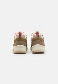 Braune und beige Sneakers mit strukturiertem Mesh, gepolsterter Kragen, roten Akzenten und einer dicken Sohle. Reflektierende Details und Branding an der Ferse.
