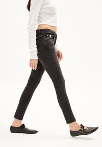 Jean skinny noir taille haute avec une texture subtile et une coupe slim. Comprend une poche avant, des passants de ceinture et un ourlet net. Associé à des ballerines noires.