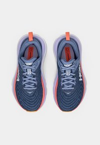 Blå träningsskor med ovandel i texturerad mesh, lila och korallfärgade detaljer, tjock sula och platta skosnören. Varumärke på sidan.