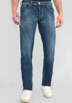 Vaqueros de mezclilla en azul oscuro con corte recto, diseño de cinco bolsillos y un desvanecimiento sutil. Combinados con zapatillas blancas.