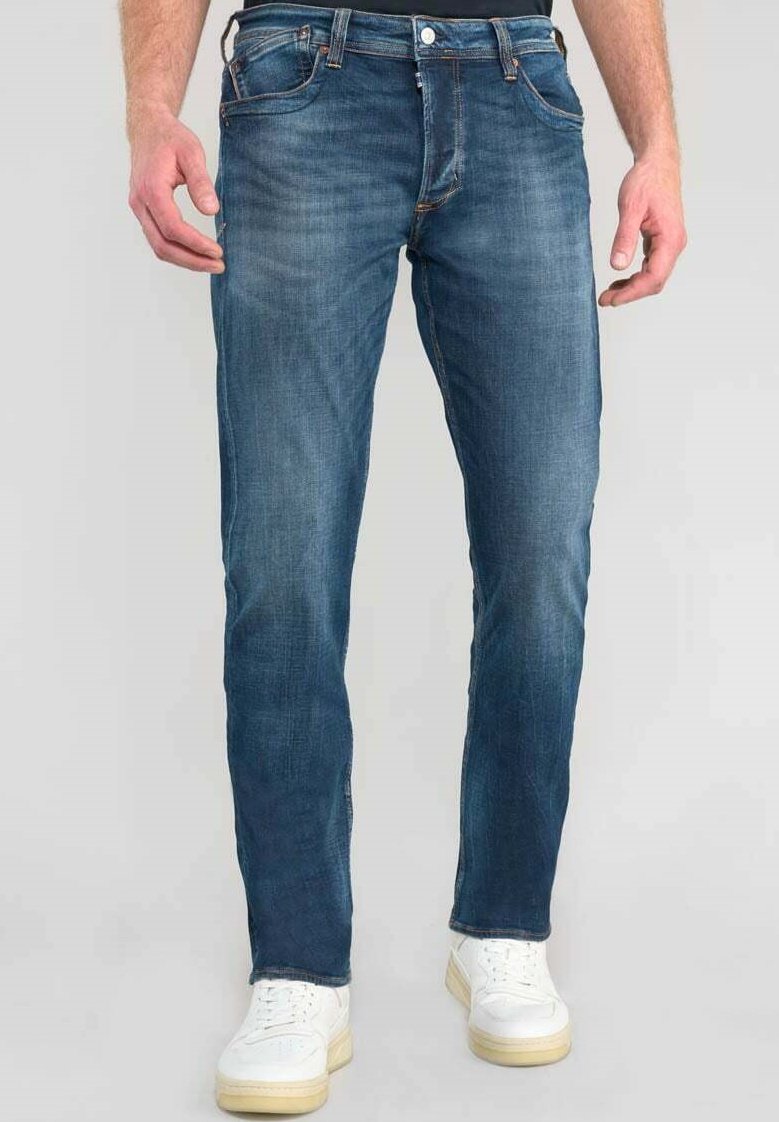 Vaqueros de mezclilla en azul oscuro con corte recto, diseño de cinco bolsillos y un desvanecimiento sutil. Combinados con zapatillas blancas.