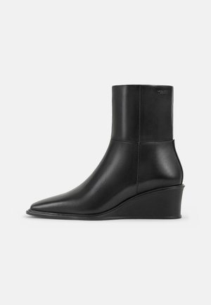 Stivaletti neri in pelle con punta a forma affilata e tacco a zeppa. Texture liscia, design aderente, senza hardware visibili o motivi.