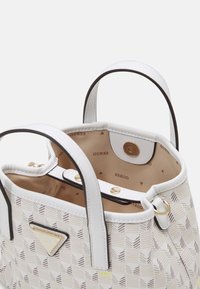 Geantă albă cu un model geometric, accesorii aurii, două mânere superioare și căptușeală din țesătură cu un design repetitiv al logo-ului.