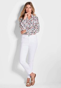 Bloemendruppel blouse met een V-hals, lange mouwen en speelse kleuren; gecombineerd met witte strakke jeans en beige sandalen met een ronde accent.