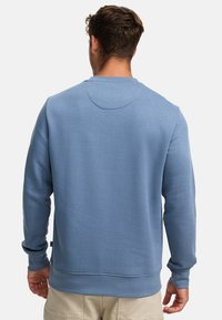 Kék crewneck pulóver, puha anyagból készült, hosszú ujjakkal és kerek nyakkal. A hátoldalon sima textúra és finom varrások találhatók.