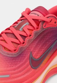 Nike tenisica za trčanje s gornjim dijelom u gradijentu ružičaste boje, teksturiranom površinom, crvenim vezicama i obućom s mekanom steljom koja ima narančaste i žute akcentne boje.