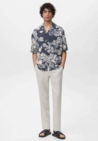 Camicia a maniche corte con bottoni, in un motivo floreale blu navy e crema, abbinata a pantaloni beige chiaro e sandali neri.