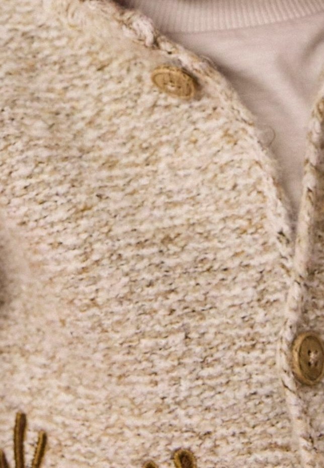 Gros plan d'un cardigan beige en tricot avec des boutons en bois sur un pull à col roulé côtelé beige clair.