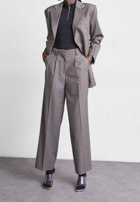 Grå skräddarsydd kostym med en strukturerad kavaj och högmidjade vida byxor. Outfiten kombineras med en svart åtsittande topp och klara klackskor.
