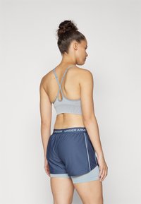Sujetador deportivo gris con tirantes cruzados y tejido que absorbe la humedad, combinado con pantalones cortos deportivos azul marino que presentan una cinturilla con logo y acentos laterales.