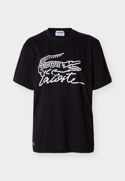 Черна тениска с къс ръкав с голям бял логотип на Lacoste, включващ стилизиран крокодил и марково име с курсив отпред.
