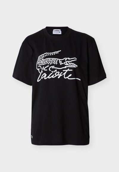 Черна тениска с къс ръкав с голям бял логотип на Lacoste, включващ стилизиран крокодил и марково име с курсив отпред.