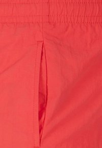 Coral fabric shorts featuring an elastic waistband and a side pocket with a vertical slit. Smooth texture and lightweight design.