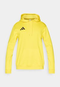 Κίτρινο φούτερ με κουκούλα και τσέπη μπροστά, κορδόνι στο καπέλο και μαύρο λογότυπο Adidas στο αριστερό στήθος. Λείο ύφασμα και ριμπ μανσέτες.