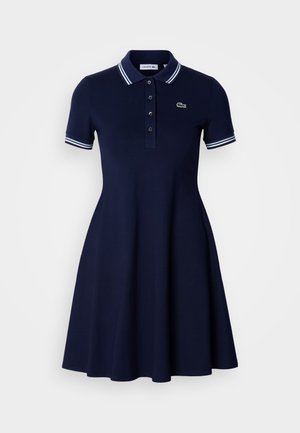 Vestido tipo polo azul marino de manga corta con cuello y puños con rayas blancas, tapeta de botones y pequeño logo bordado en el pecho.