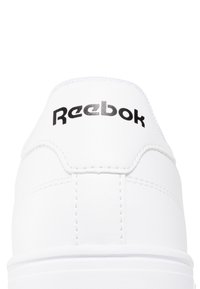 Valkoinen nahkakenkä, jossa on pyöreä muotoilu. Varustettu pehmustetulla nilkkaremmillä ja mustalla "Reebok"-logolla kantapäässä. Saumojen yksityiskohdat näkyvissä.