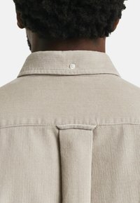 Beiger Corduroy-Hemdkragen mit einem einzelnen Knopf auf der Rückseite. Verfügt über eine vertikale Rippstruktur und Nahtdetails entlang der Schultern.