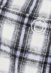 Plaid fabric in white, black, and lavender, featuring a soft, textured finish and a stitched logo. Distinct pattern with contrasting lines.