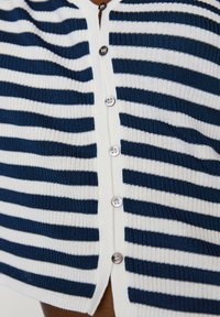 Granatowo-biały sweter w paski o dzianinowej teksturze, z pięcioma guzikami z przodu i lekko skróconym fasonem.