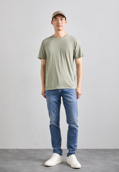 T-shirt vert clair à manches courtes, jeans bleus et baskets blanches. Texture captivante avec une coupe décontractée et sans motifs ni accents visibles.