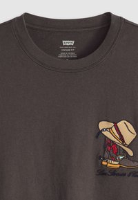 Sudadera de algodón gris oscuro con un bordado colorido de una bota y un sombrero de vaquero en el lado izquierdo del pecho. Cuello redondo de canalé y corte vintage.