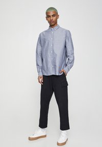 Overhemd met knopen van lichtblauwe chambray-stof, lange mouwen en een klassieke kraag, gecombineerd met zwarte cargobroek en witte sneakers.