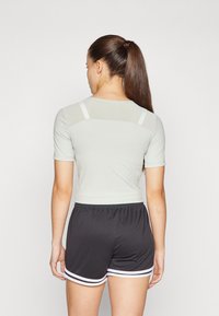 Lys grå treningstopp med korte ermer og meshdetaljer på baksiden, kombinert med sorte shorts med hvite striper langs kanten.