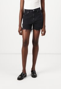 Shorts de mezclilla negra con bordes deshilachados, diseño de tiro alto, estilo de cinco bolsillos y sutil detalle de la marca en los bolsillos.