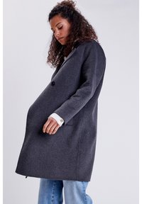 Abrigo de lana gris con diseño de doble botonadura, dos bolsillos laterales y botones. Presenta un acabado texturizado y puños en blanco contrastante.