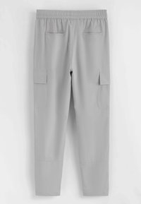 Pantalon cargo gris clair avec taille élastique, deux poches fendues à l'arrière et deux poches à rabat sur les côtés, suspendu sur un fond blanc.