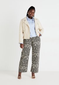 Chaqueta de imitación de cuero beige, camisa de botones a rayas azules, pantalones anchos de estampado de cebra en blanco y negro, sandalias doradas de punta abierta.