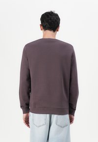 Genser med hette i mørk mauve, laget av mykt materiale. Har rund hals, lange ermer og ribbede mansjetter og nederkant. Ingen synlige logoer.
