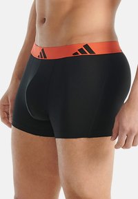 Zwarte boxer shorts met een contrasterende oranje elastische tailleband met zwarte adidas-logo's. Glad textuur en een aansluitend ontwerp.
