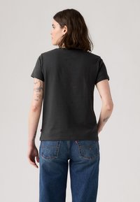 Mørk grå bomulls t-skjorte med korte ermer, rund hals, enkel design. Kombinert med blå denim jeans med stikning detaljer på baklommen.