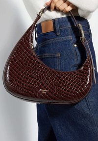 Maroon handbag with a textured, glossy finish, featuring a curved shape and a short strap. Includes subtle logo detailing on the front.