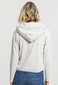 Lys grå hettegenser med avslappet passform, myk tekstur og sydd kant, parret med blå jeans, vist fra baksiden.