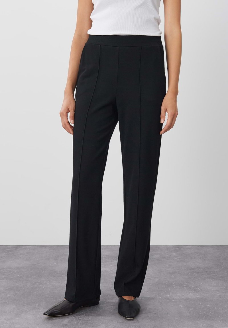 Pantaloni neri su misura realizzati in tessuto morbido, con vita alta, cuciture frontali e design a gamba dritta. Indossati con scarpe flat a punta.
