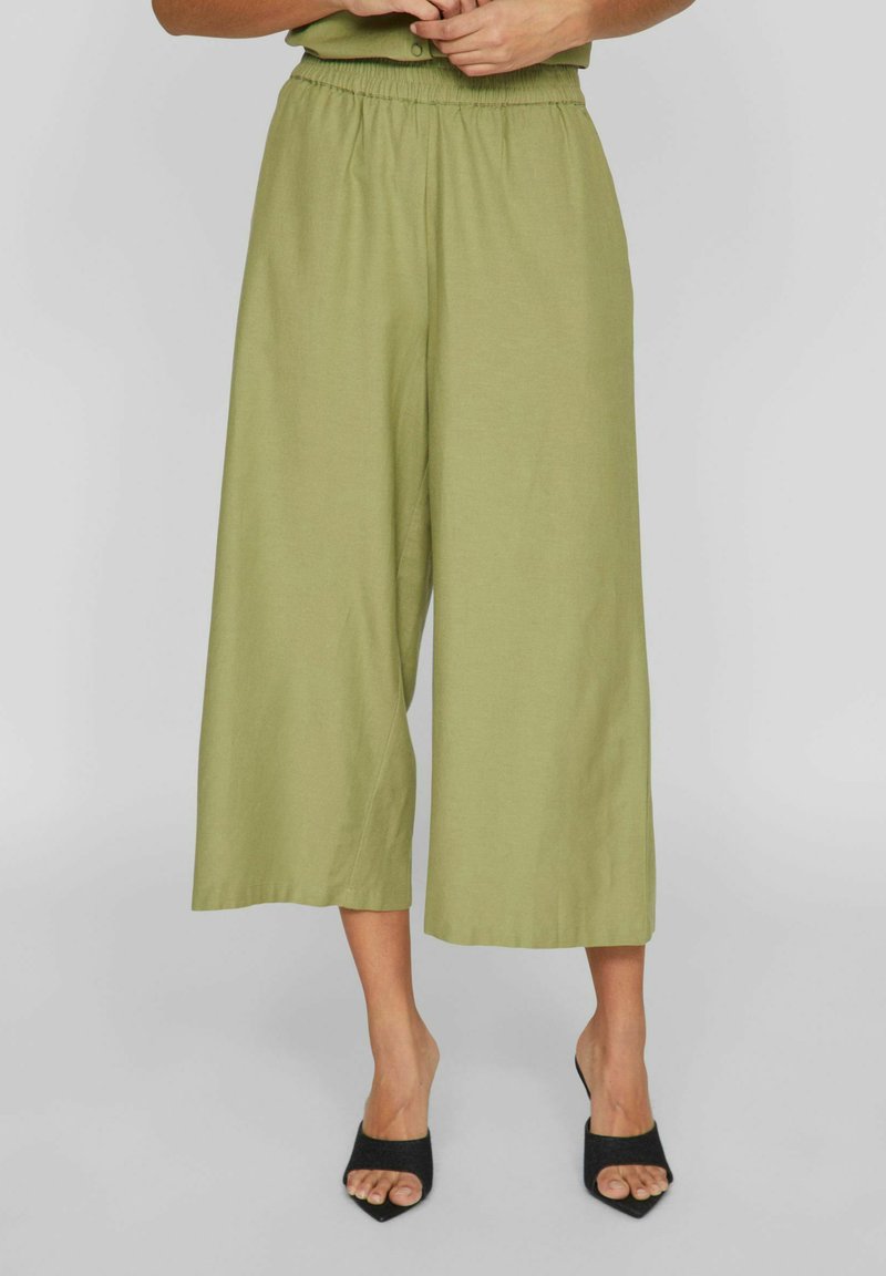 Culottes vert clair, à jambes larges et taille élastique. Tissu doux avec une texture lisse. Associés à des escarpins noirs à bout pointu.