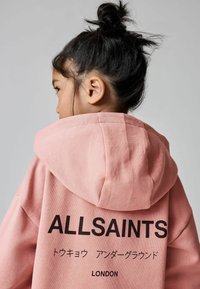 Roza dukserica s kapuljačom koja na leđima ima veliki crni logo "ALLSAINTS", uz dodatni tekst na japanskom i "LONDON" na dnu.