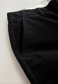 Black corduroy pants with a textured surface, featuring front pockets and a waistband with a contrasting white interior.