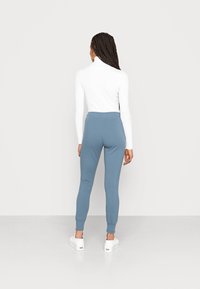 Light blue leggings with a fitted design, elastic waistband, and tapered cuffs, paired with a white ribbed turtleneck. Simple and functional.