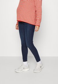 Pullover de malha às riscas vermelhas e brancas, jeans skinny azul escuro e ténis brancos de desporto. Os detalhes incluem punhos e um design ajustado.