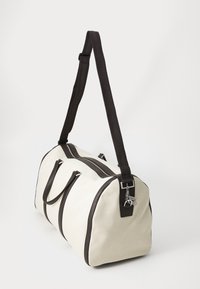 Borsa da viaggio in tela beige con accenti marrone scuro, doppio manico superiore, tracolla regolabile e chiusura lampo in metallo argentato.