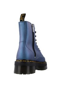 Bottes en cuir bleu, à la cheville, avec une finition brillante, une semelle noire épaisse, une fermeture éclair sur le côté et des coutures jaunes le long de la semelle.