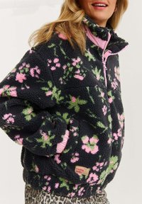 Námořnický flísový pulover s květinovým vzorem v růžové a zelené barvě, vysokým límcem, zipem a žebrovanými manžetami. Štítek nese nápis "Cítím se šťastně."