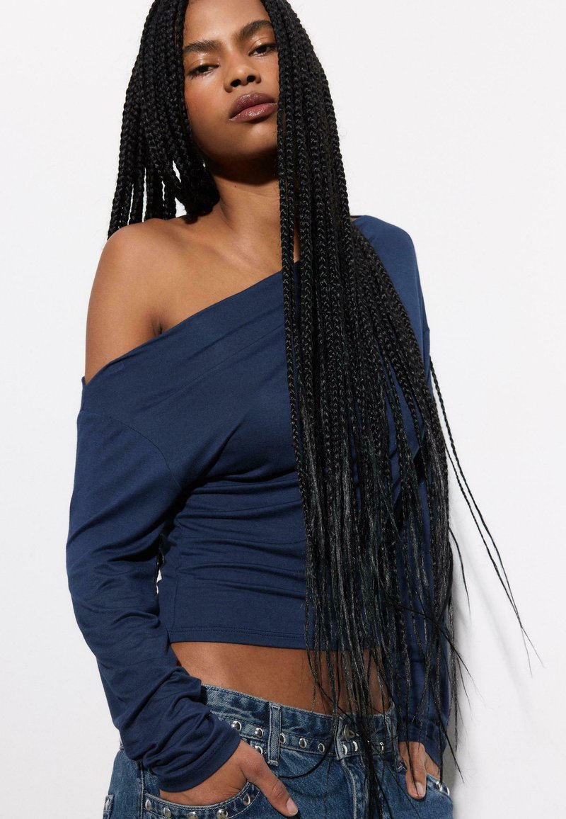 Haut à manches longues bleu marine avec une épaule dégagée, en tissu doux, présentant une coupe ajustée et une texture qui tombe confortablement.