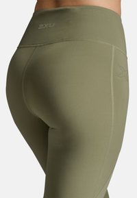 Olivgrüne Leggings mit hoher Taille, glattem Stoff und tonal abgestimmtem Logo-Detail. Entworfen für Komfort und Flexibilität.